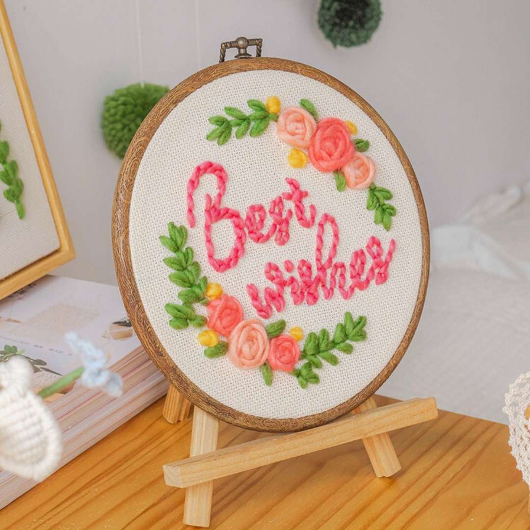 Best Wishes needle punch kit embroidery displayed on a wooden stand, showcasing a beautiful floral design with pink and green accents