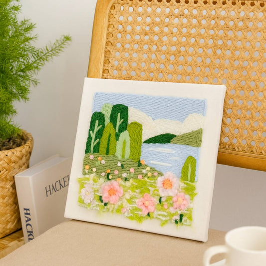 Punch needle embroidery kit  landscape art piece on a wooden chair with books and a plant in the background.
