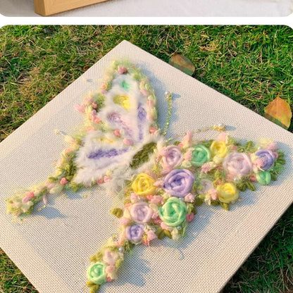 Puddingcase punch needle kit featuring a butterfly with pastel floral accents, displayed on grass, ideal for DIY embroidery and creative crafting.